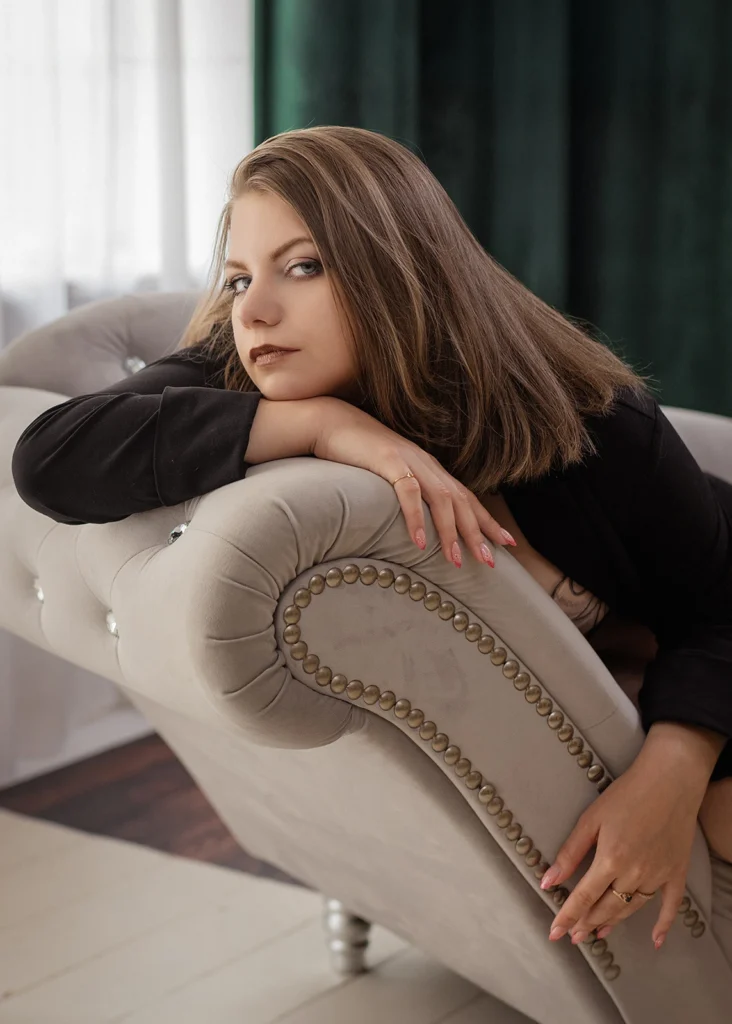 Sesja kobieca – portret kobiety opartej na jasnej kanapie, w czarnej stylizacji.