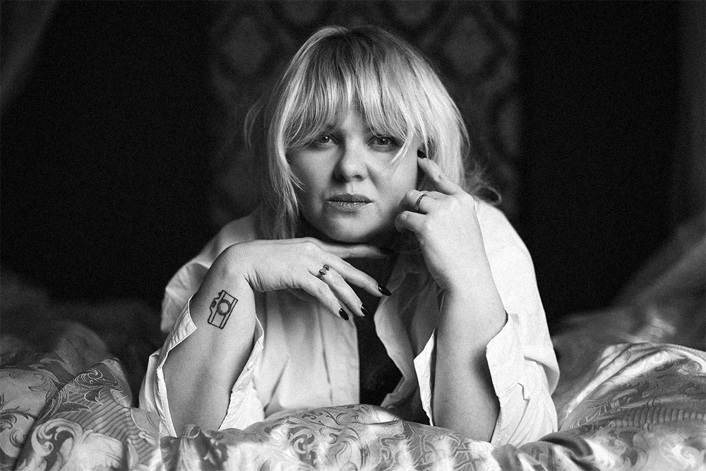 Czarno-biały portret kobiecy Marty w białej koszuli, leżącej na wzorzystych poduszkach w studio.